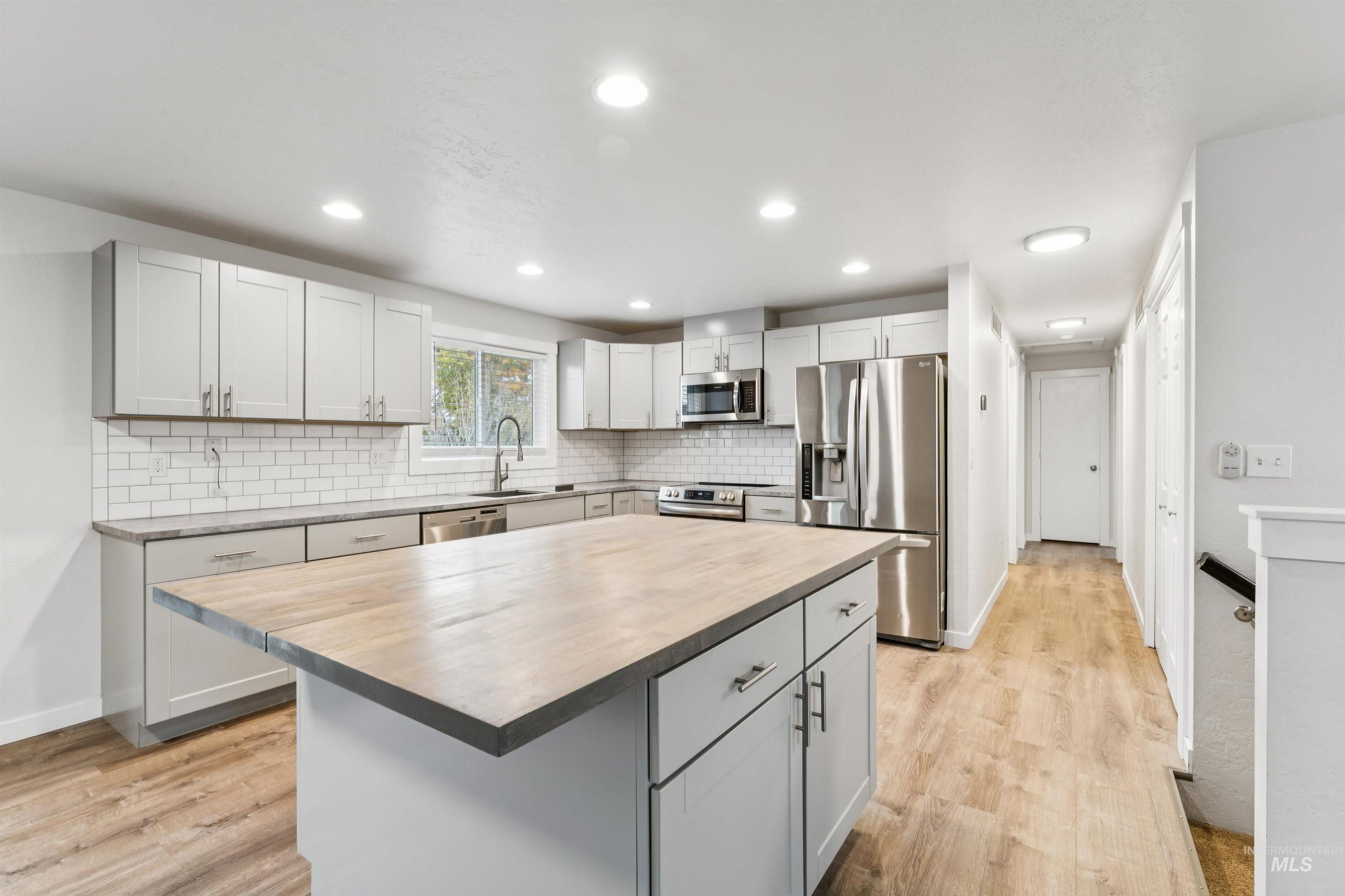 Kitchen with stainless steel appliances, light wood-style flooring, a center island, tasteful backsplash, and recessed lighting