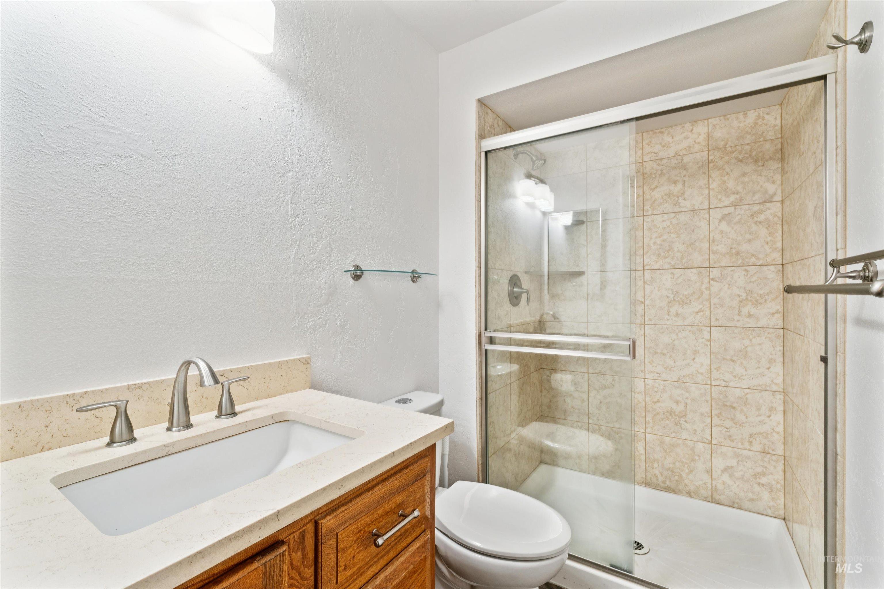 Full bath with vanity, a textured wall, and a stall shower