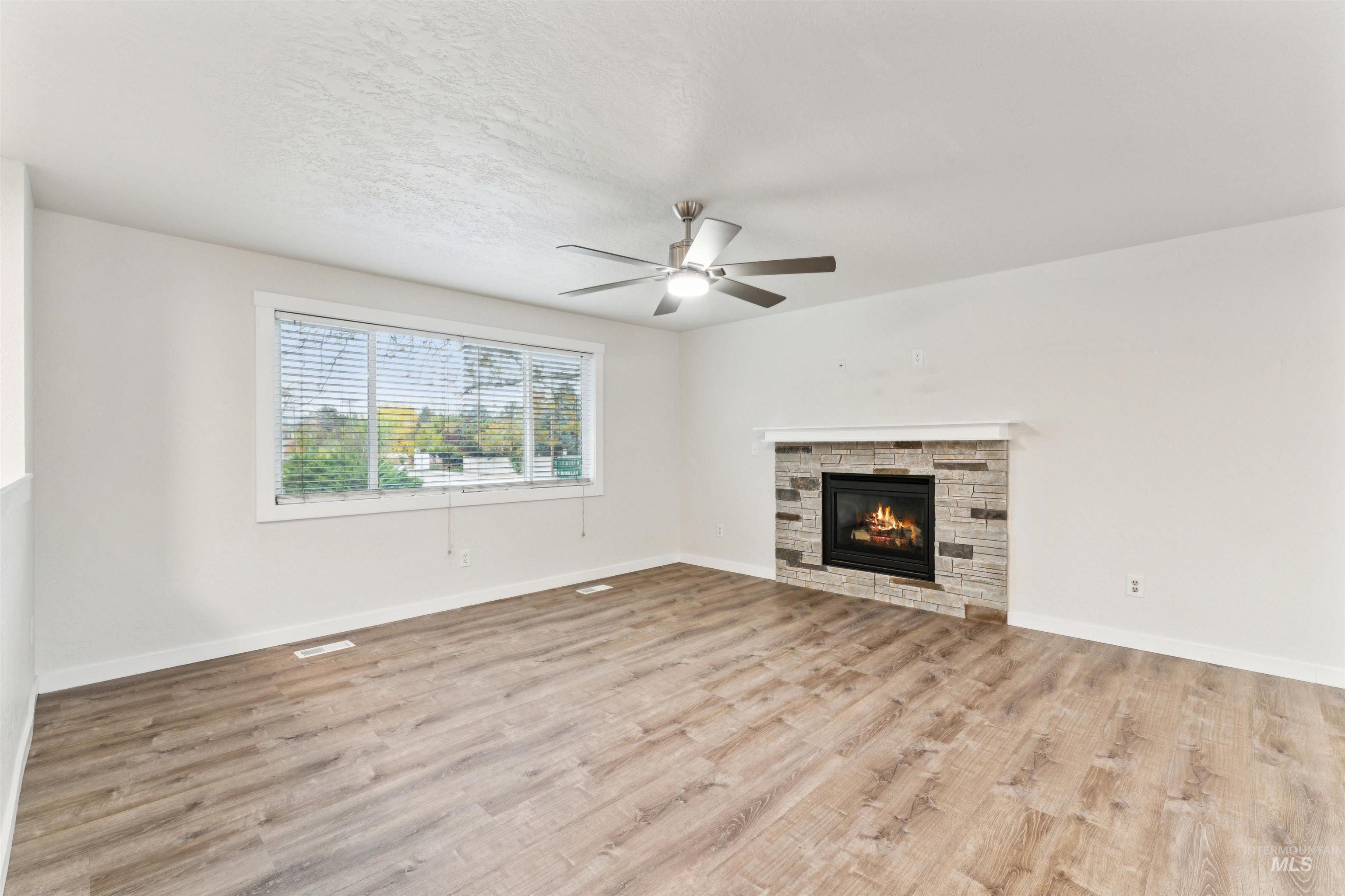Unfurnished living room featuring a stone fireplace, light wood-type flooring, a ceiling fan, and a textured ceiling