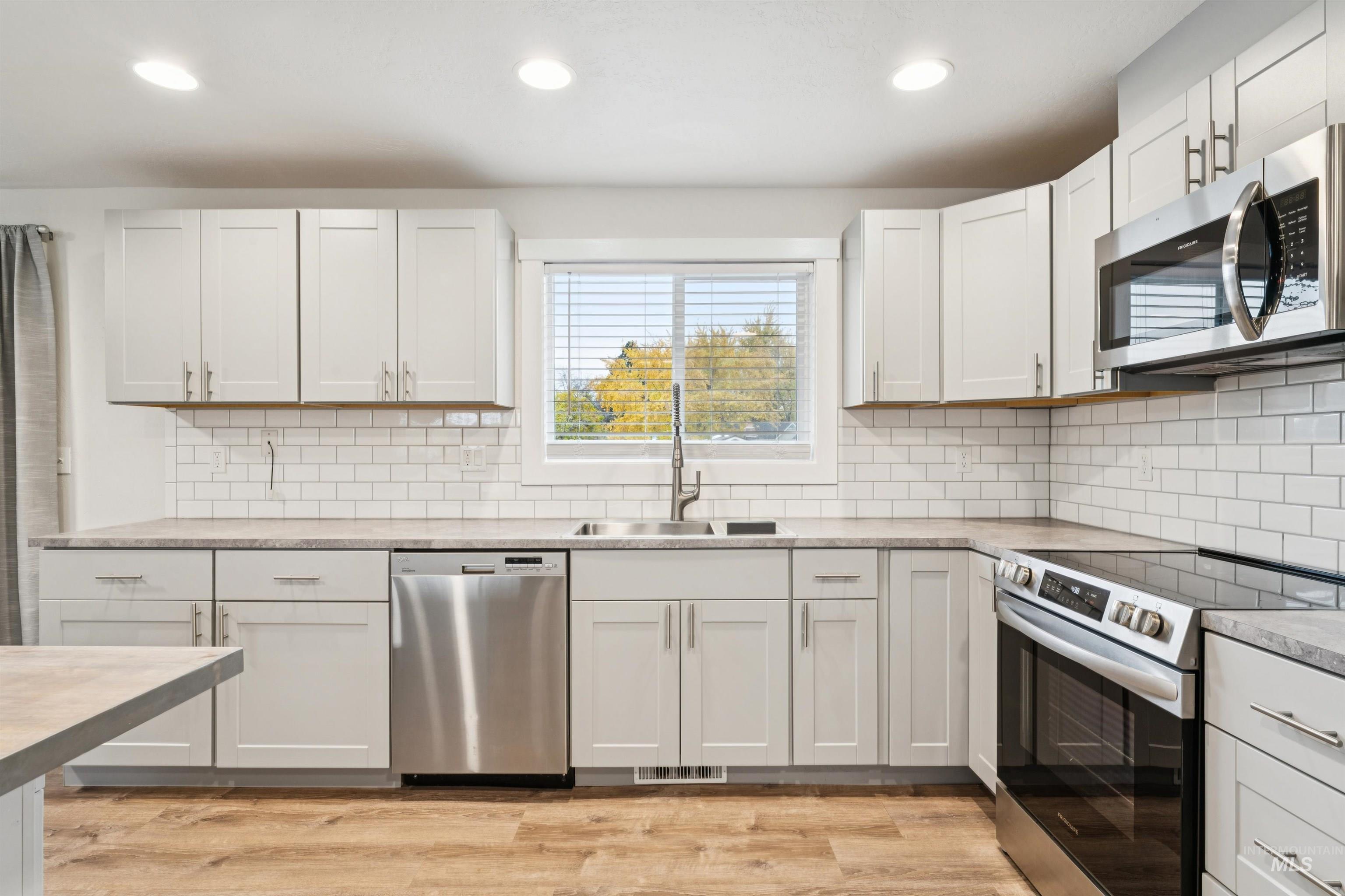 Kitchen with stainless steel appliances, light wood finished floors, white cabinets, recessed lighting, and backsplash