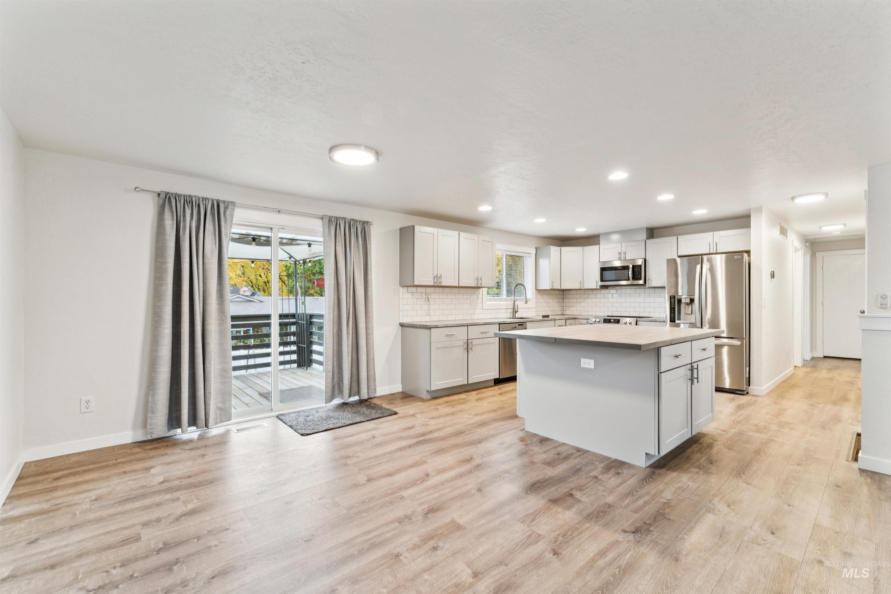 Kitchen featuring stainless steel appliances, light countertops, a kitchen island, tasteful backsplash, and light wood-type flooring