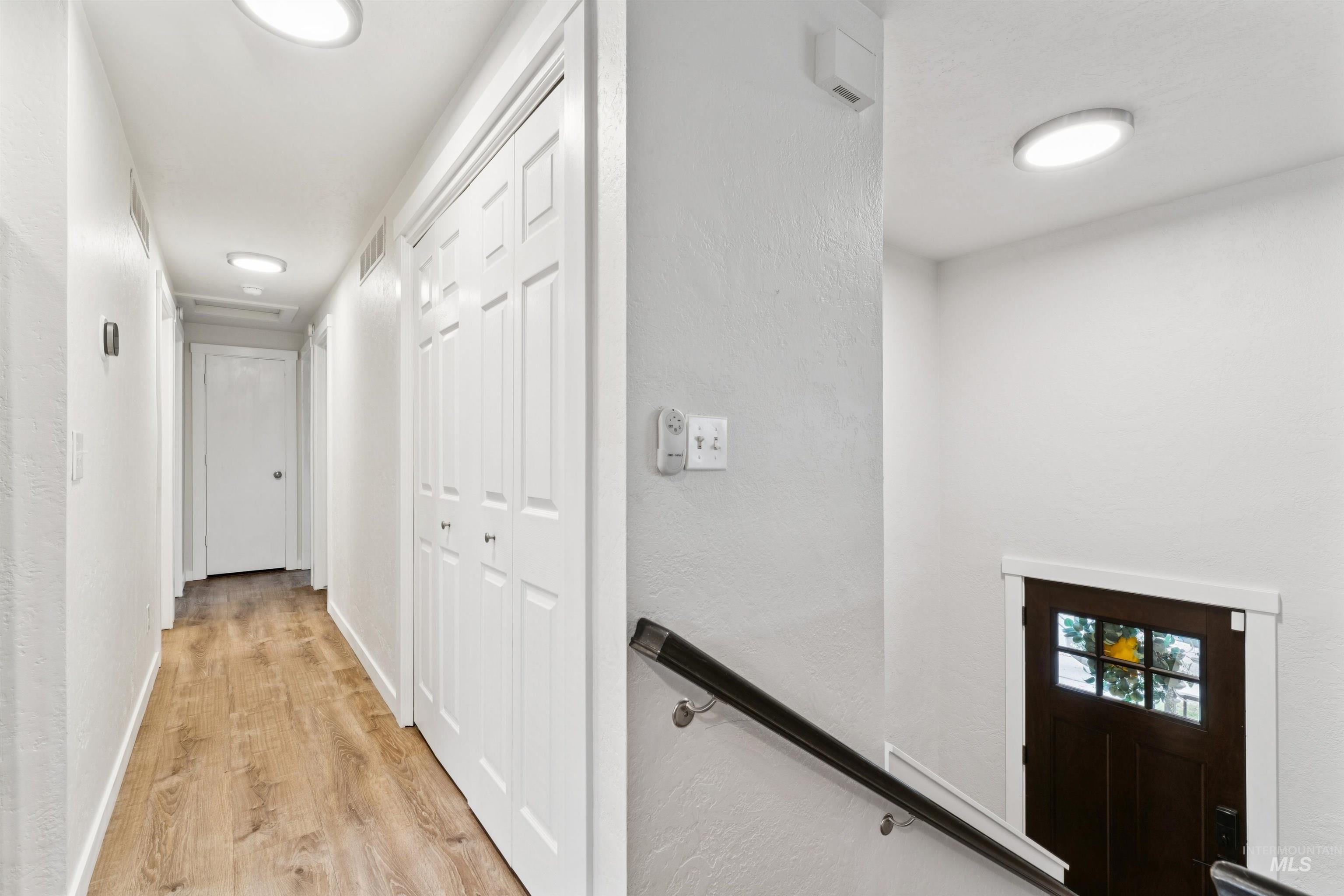 Corridor featuring light wood finished floors, a textured wall, and an upstairs landing