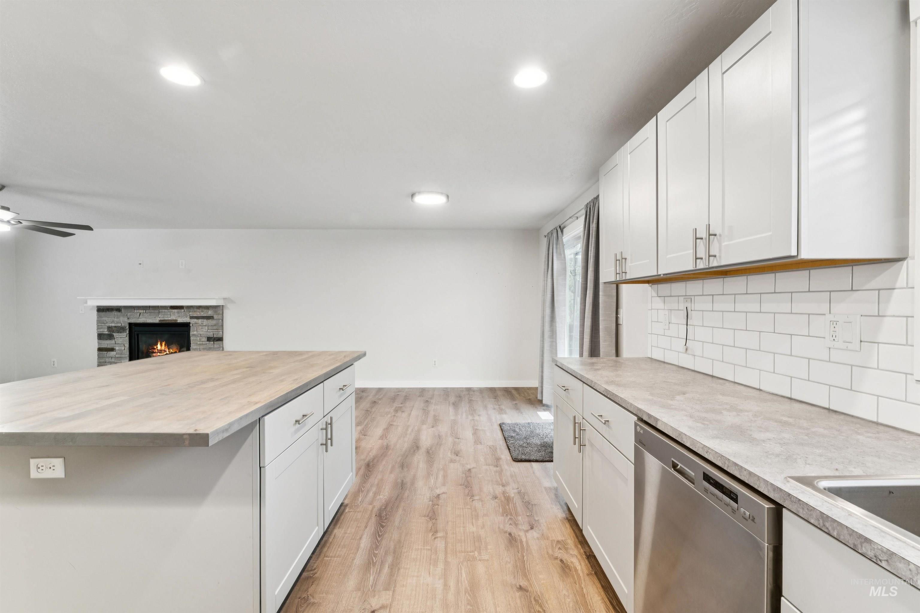 Kitchen featuring light countertops, dishwasher, a stone fireplace, white cabinets, and recessed lighting