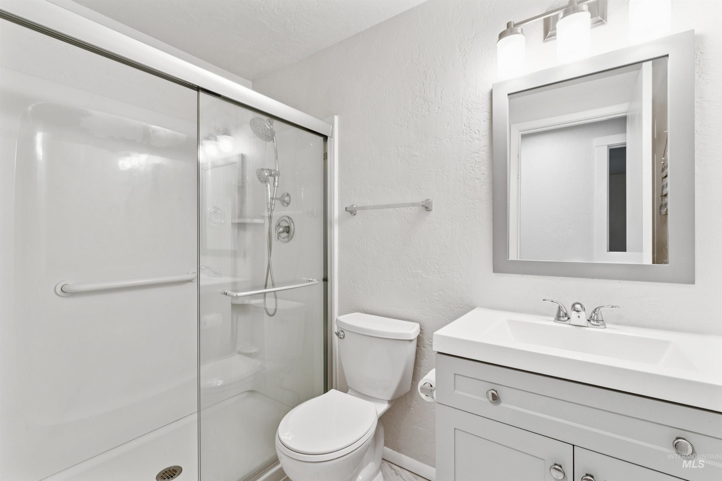 Bathroom with a textured wall, vanity, and a shower stall