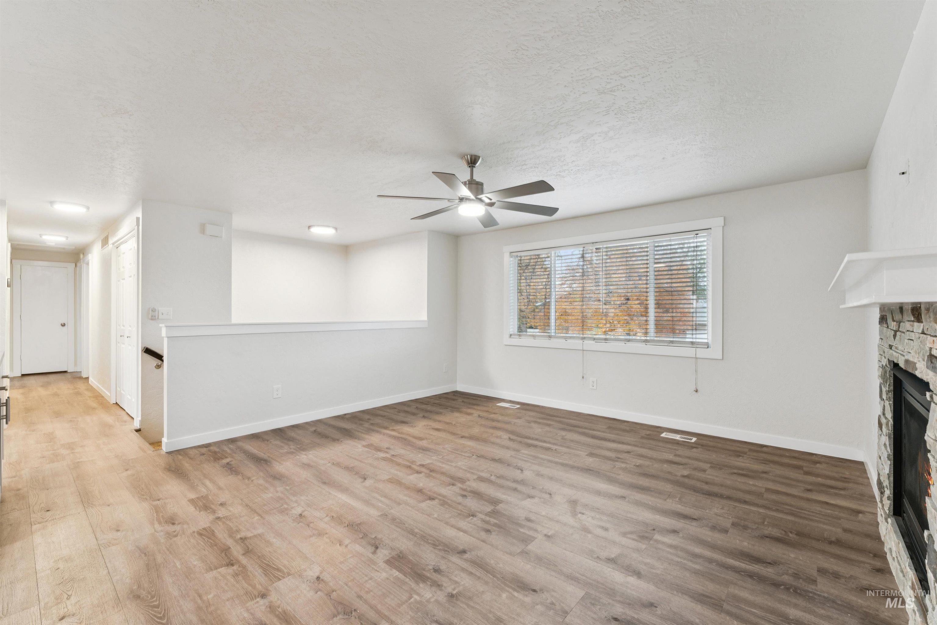Unfurnished living room with a fireplace, wood finished floors, a textured ceiling, and ceiling fan