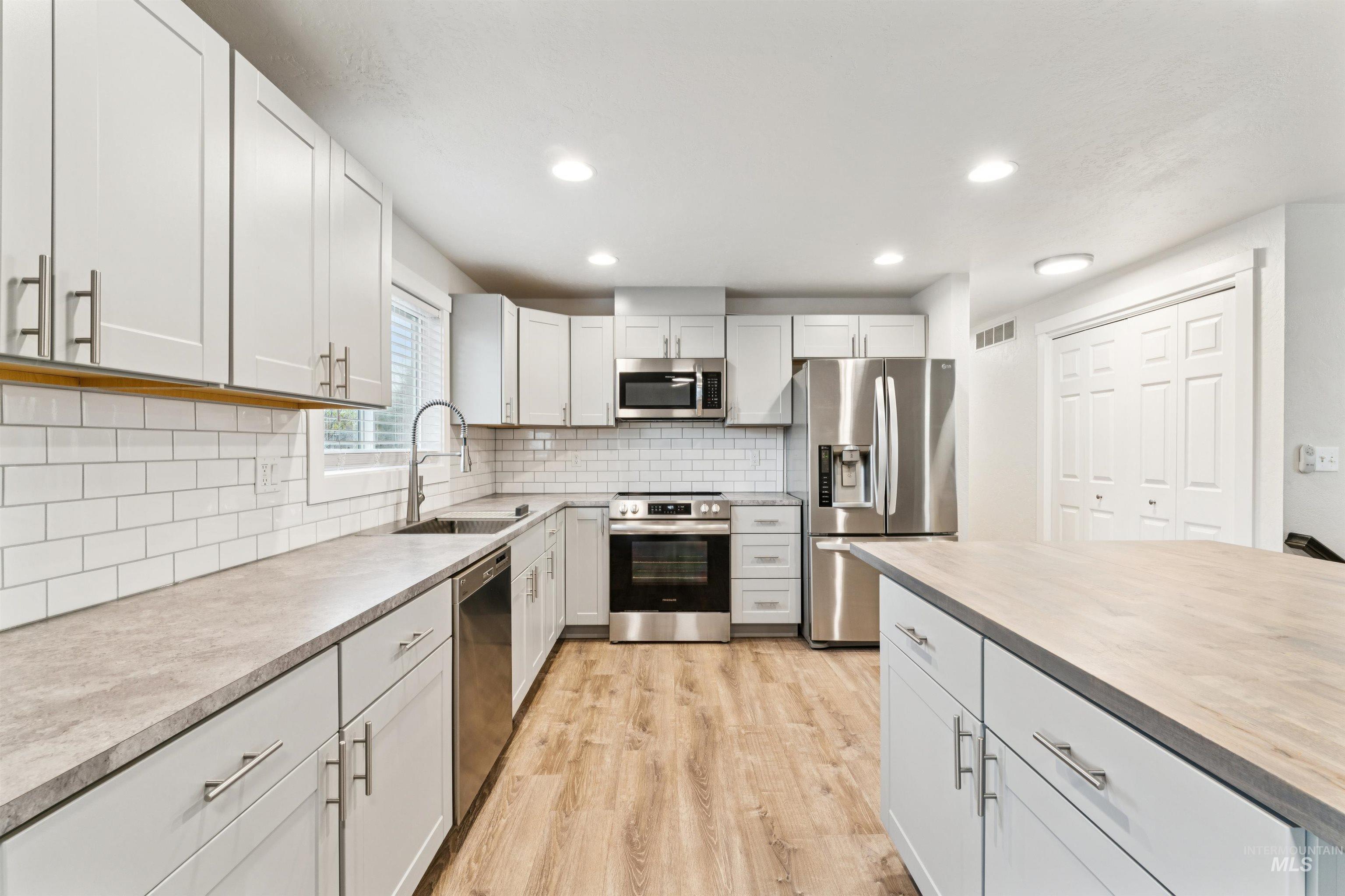 Kitchen with stainless steel appliances, backsplash, recessed lighting, light wood-type flooring, and butcher block countertops