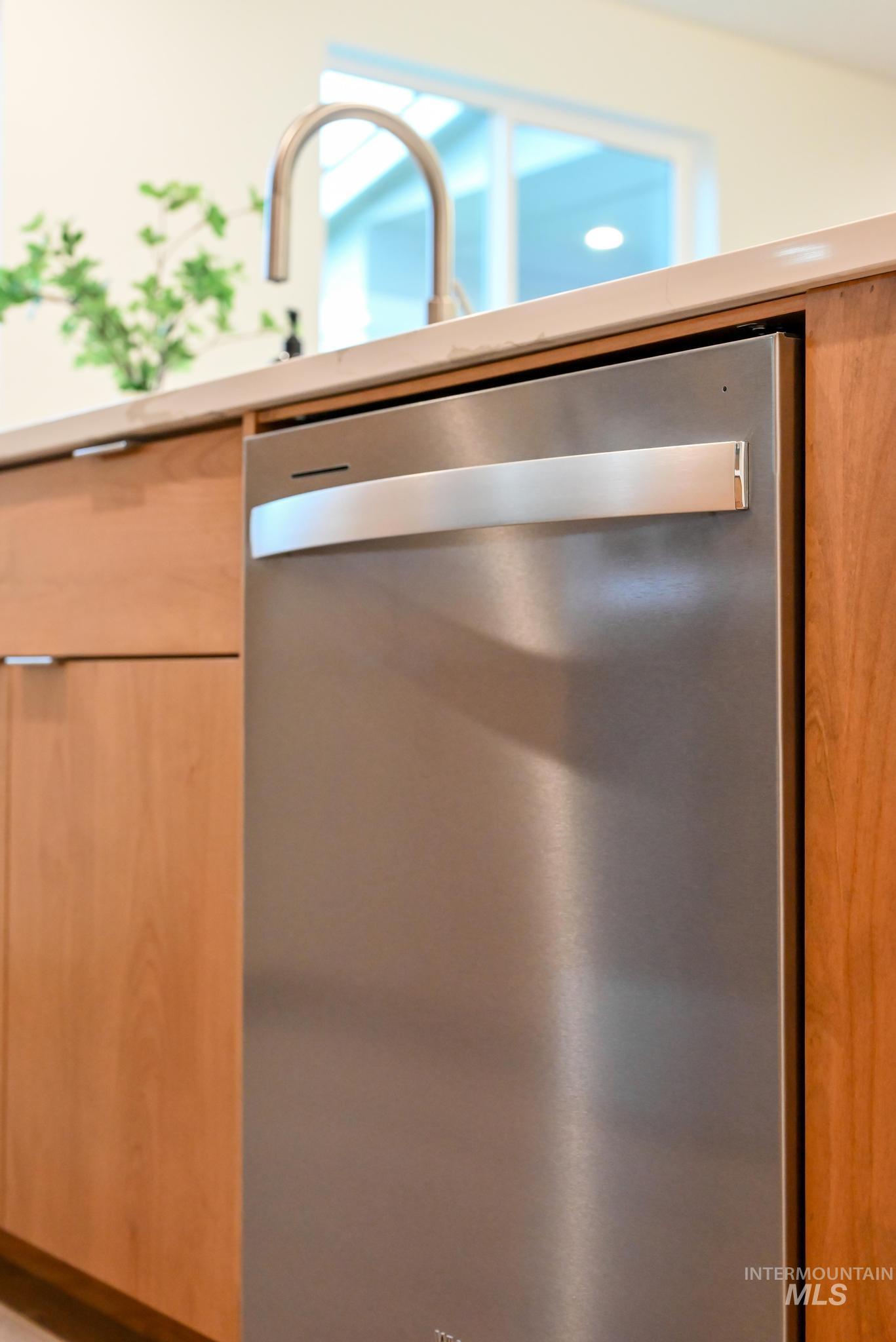 Kitchen view of dishwasher, modern cabinets, light brown cabinetry, and light countertops