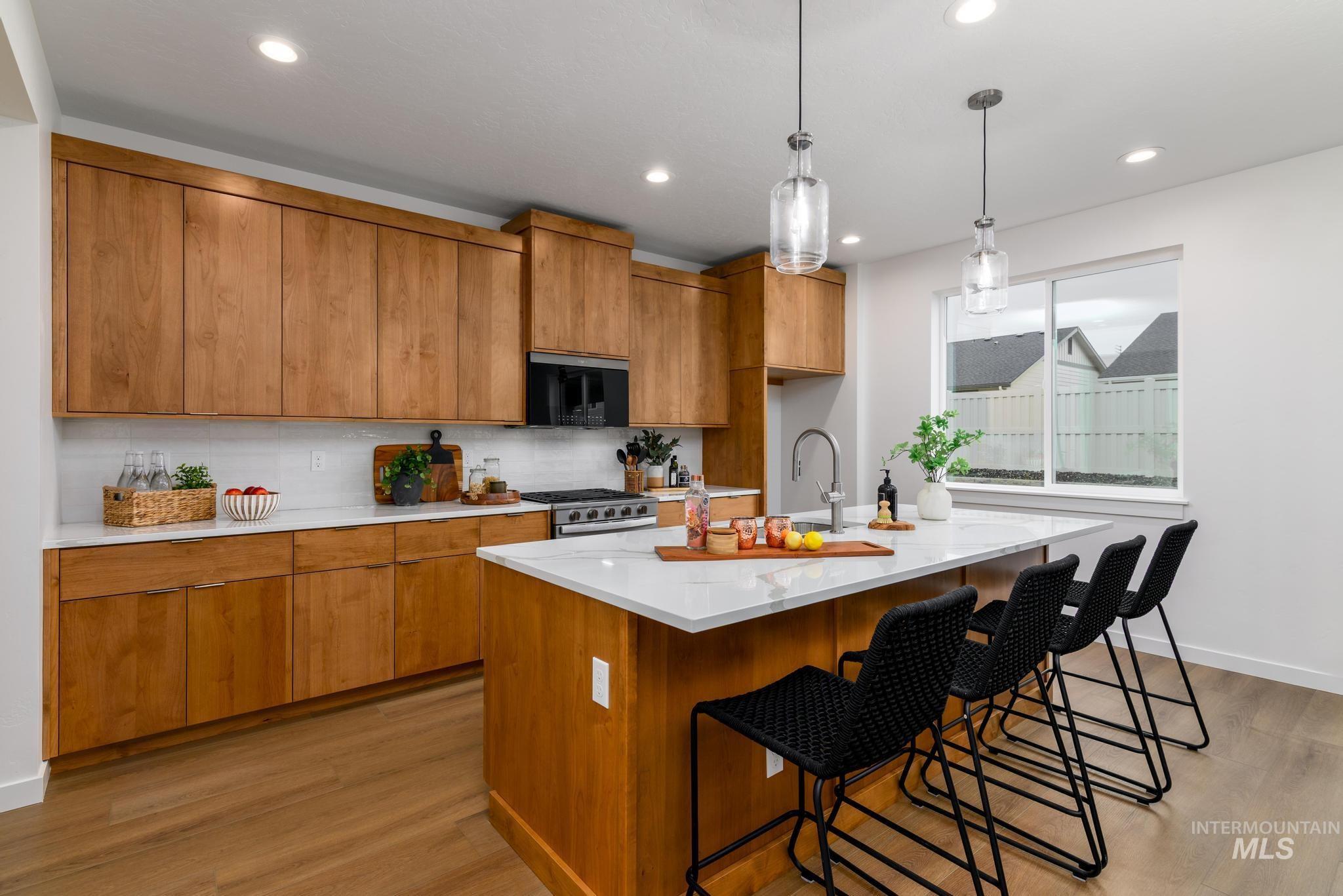 Kitchen featuring brown cabinetry, light wood finished floors, a center island with sink, tasteful backsplash, and a breakfast bar area