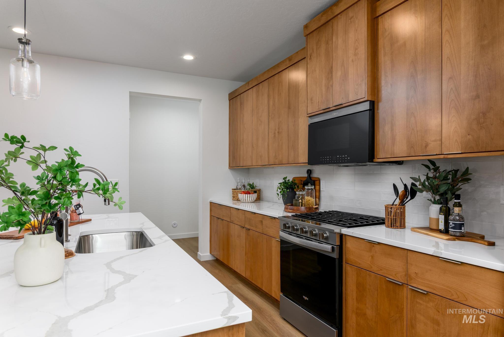 Kitchen with stainless steel gas range oven, light wood-style floors, decorative light fixtures, decorative backsplash, and black microwave
