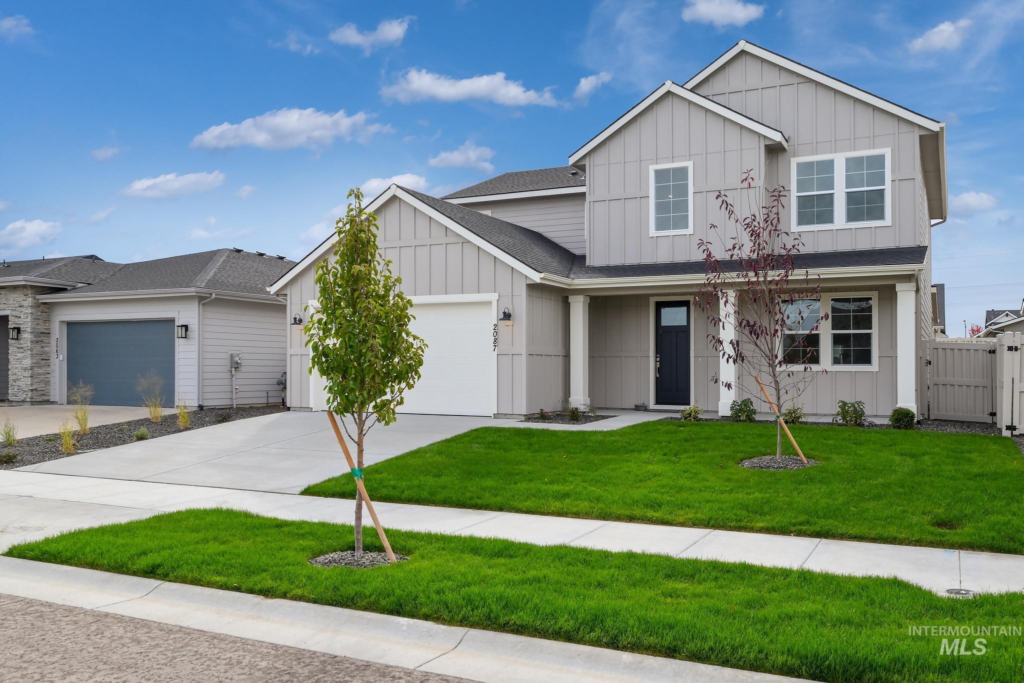 View of front of home with board and batten siding, driveway, an attached garage, and a gate