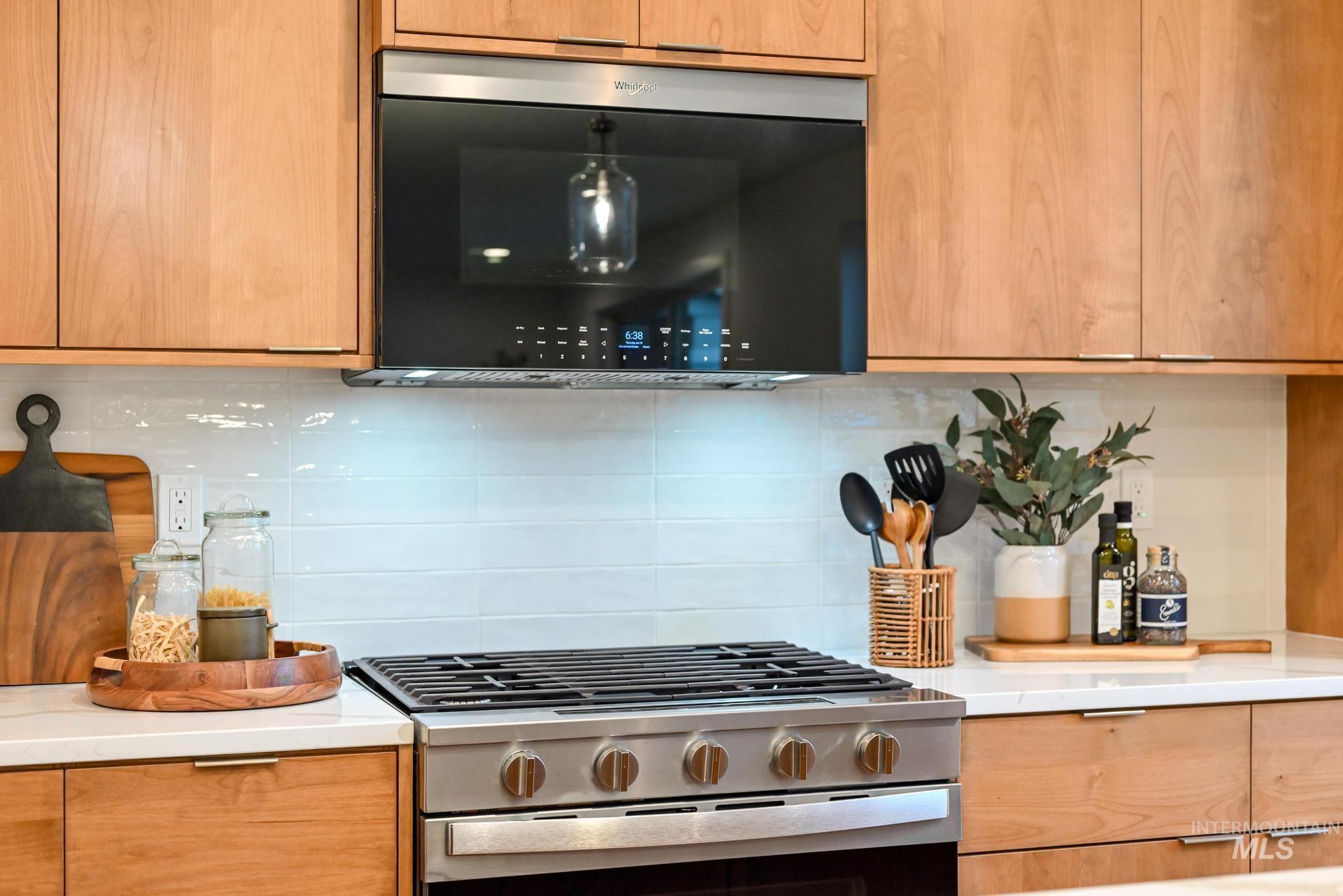 Kitchen with stainless steel gas stove, decorative backsplash, black microwave, light stone countertops, and modern cabinets