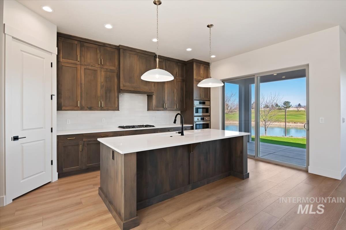 Kitchen featuring pendant lighting, backsplash, light wood-type flooring, and dark wood finish cabinetry