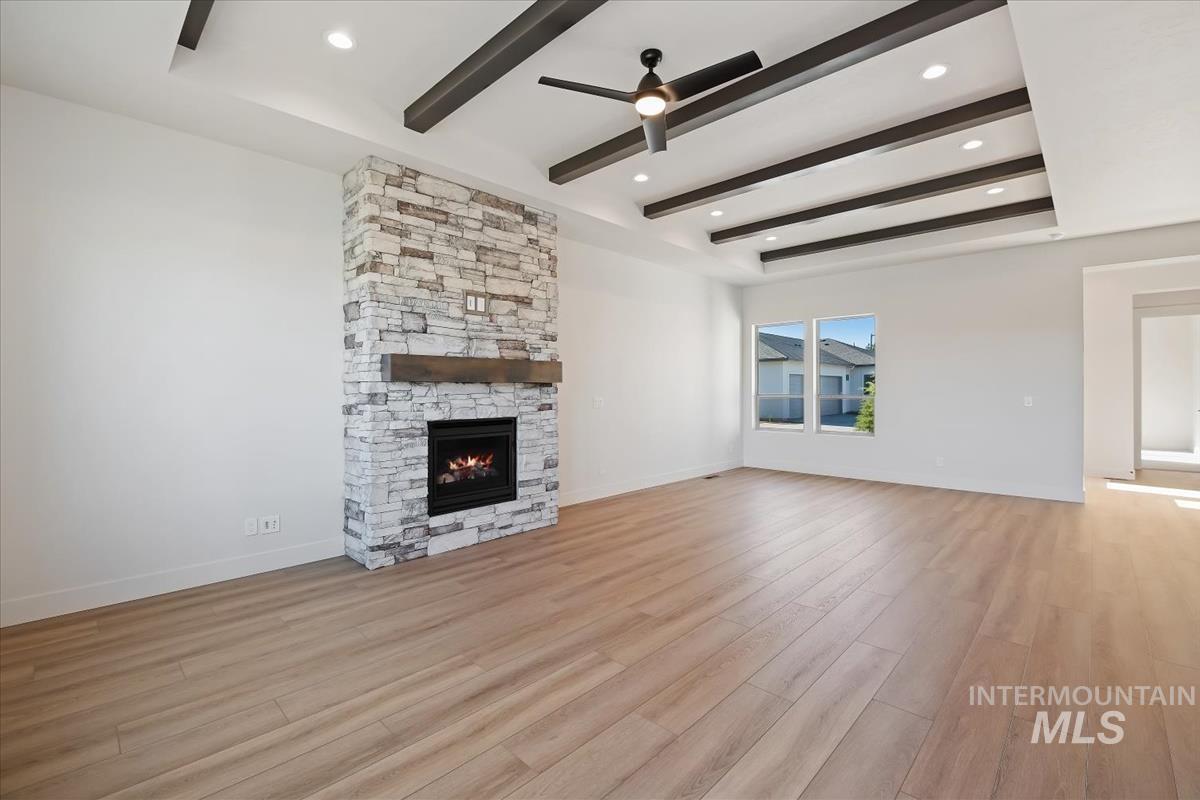 Unfurnished living room with a stone fireplace, light wood-type flooring, beam ceiling, a ceiling fan, and recessed lighting