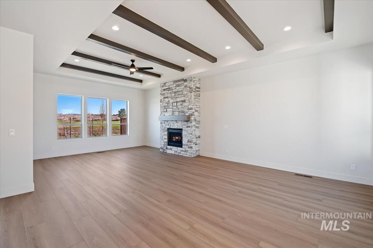 Unfurnished living room with beam ceiling, light wood-style floors, a fireplace, ceiling fan, and a raised ceiling