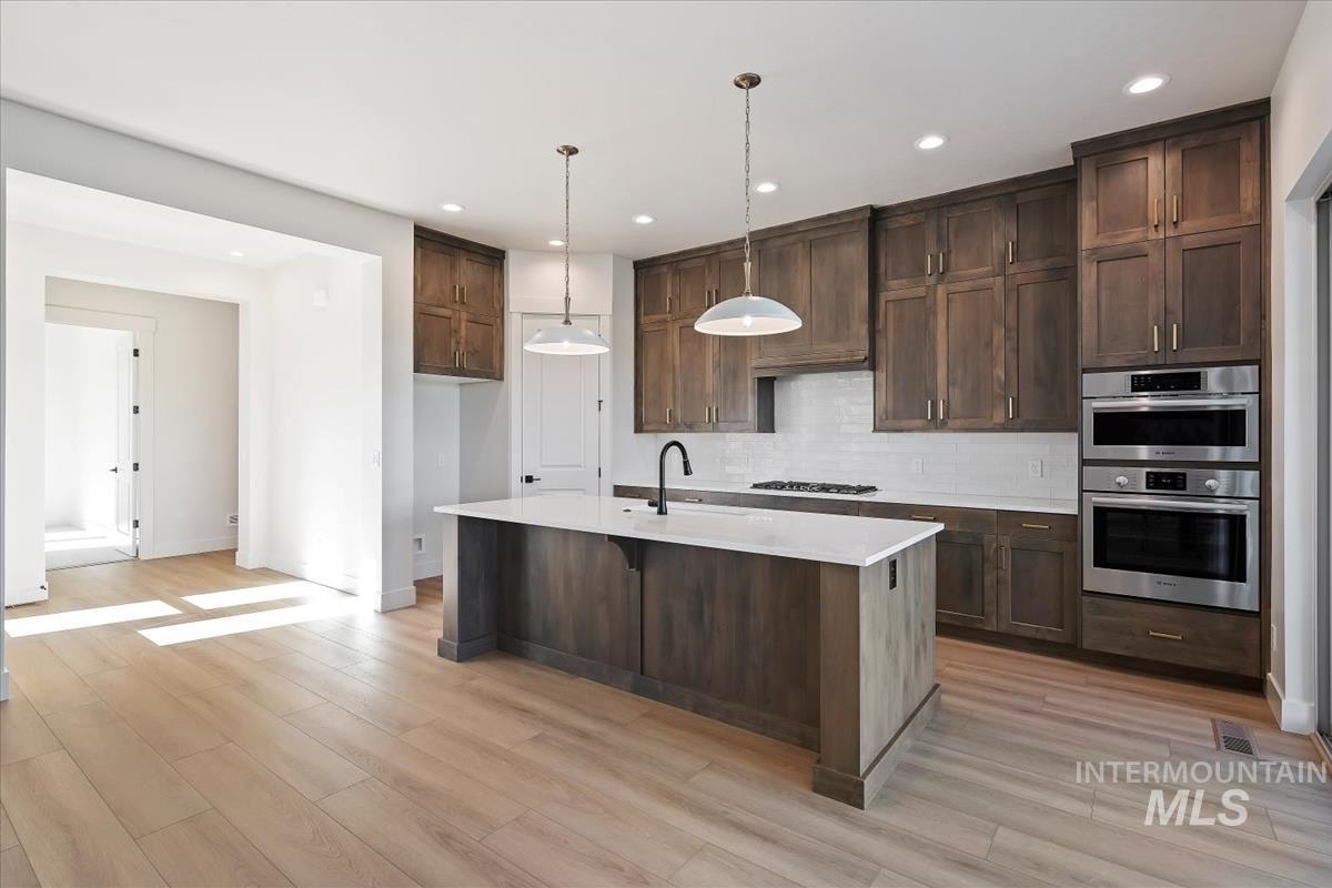 Kitchen featuring pendant lighting, light stone counters, stainless steel appliances, a kitchen breakfast bar, and a center island with sink