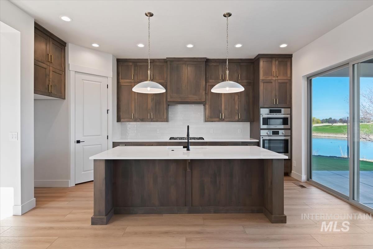 Kitchen with dark wood finish cabinets, light stone countertops, decorative light fixtures, and a kitchen island with sink