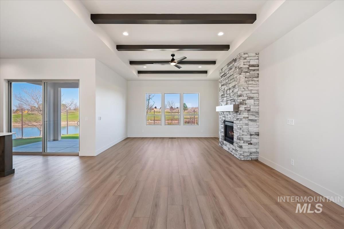 Unfurnished living room with a ceiling fan, beamed ceiling, a fireplace, light wood-style floors, and a water view
