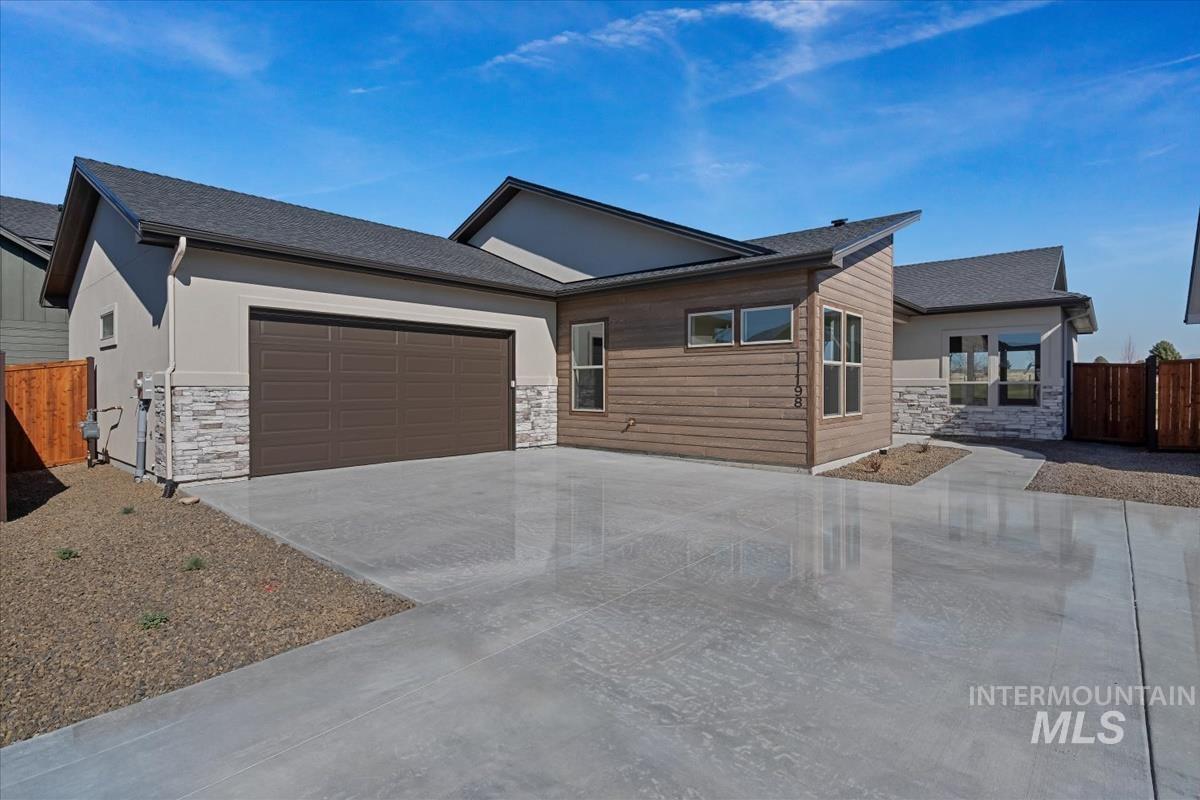 View of front of property featuring stone siding, a garage, concrete driveway, and roof with shingles