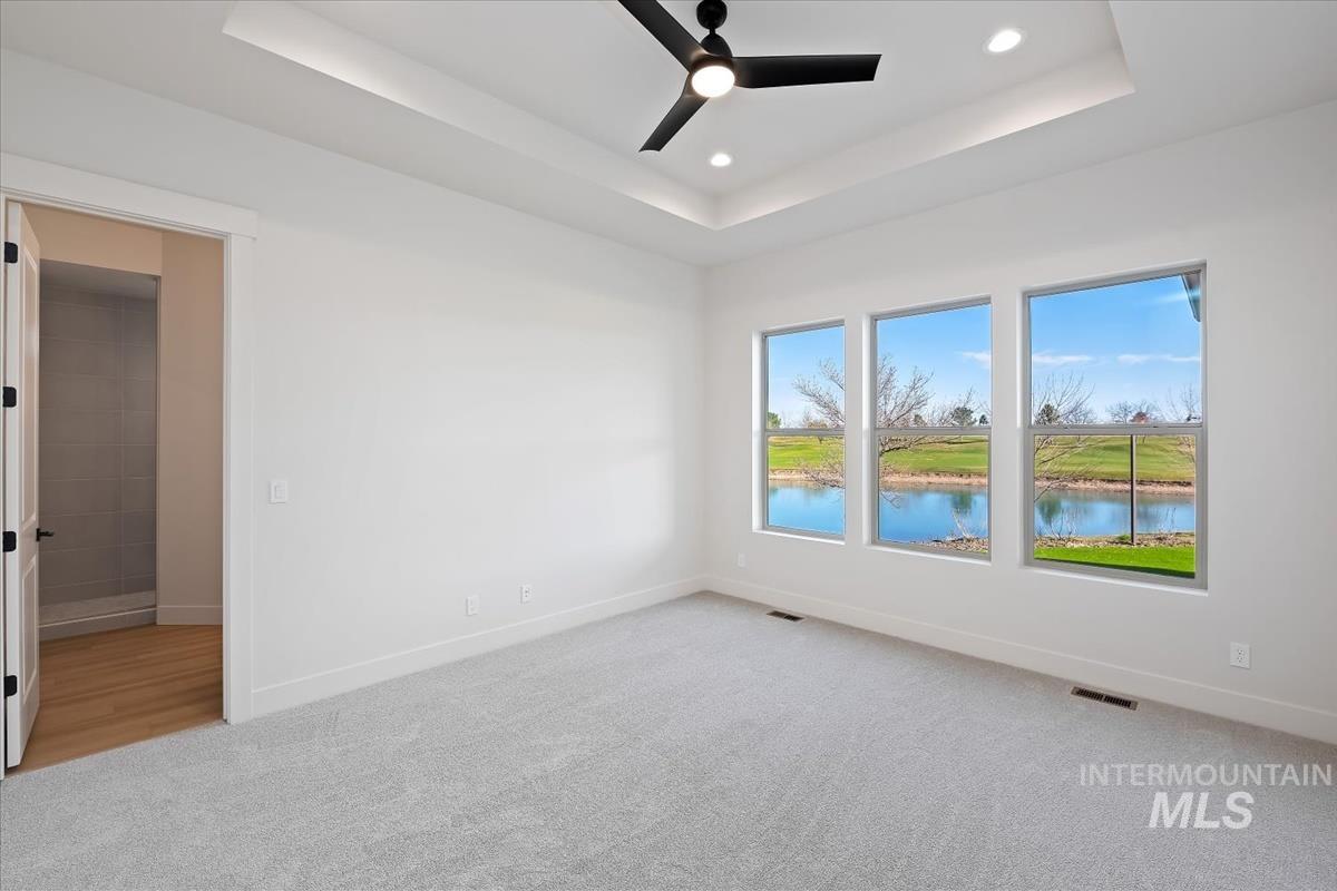 Unfurnished room featuring light carpet, recessed lighting, ceiling fan, a raised ceiling, and a water view