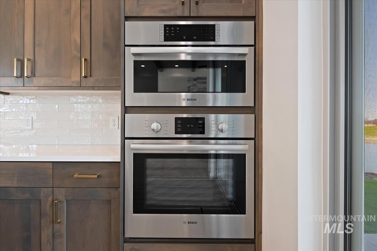 Kitchen with dark wood finish cabinetry, stainless steel double oven, and decorative backsplash