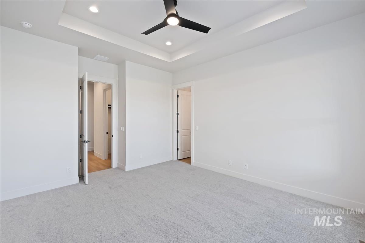 Unfurnished bedroom with a tray ceiling, light carpet, a ceiling fan, and recessed lighting