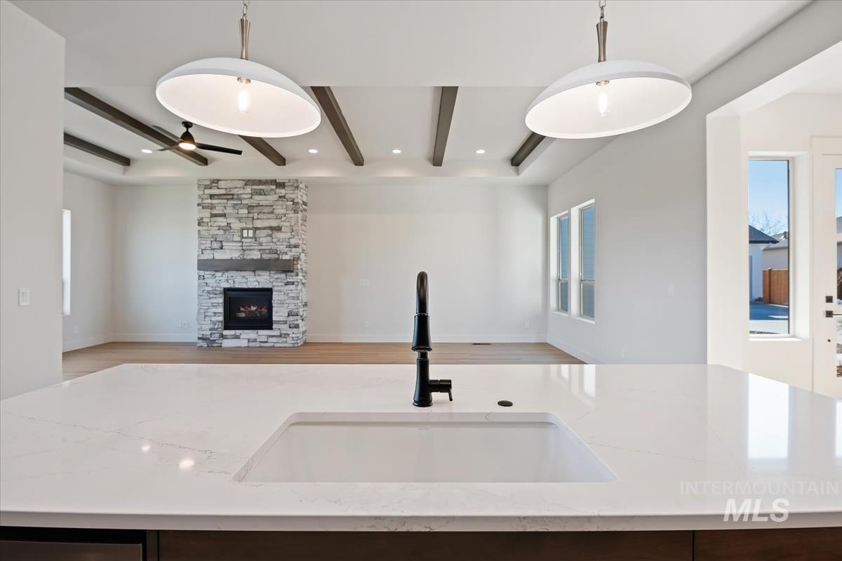 Kitchen featuring a center island with sink, a stone fireplace, open floor plan, light stone countertops, and beam ceiling