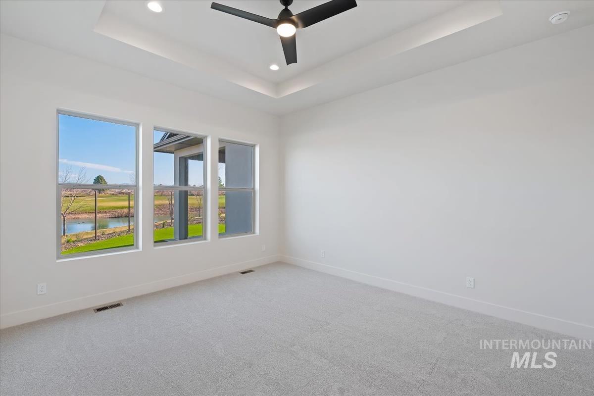 Carpeted spare room with a water view, ceiling fan, recessed lighting, and a raised ceiling