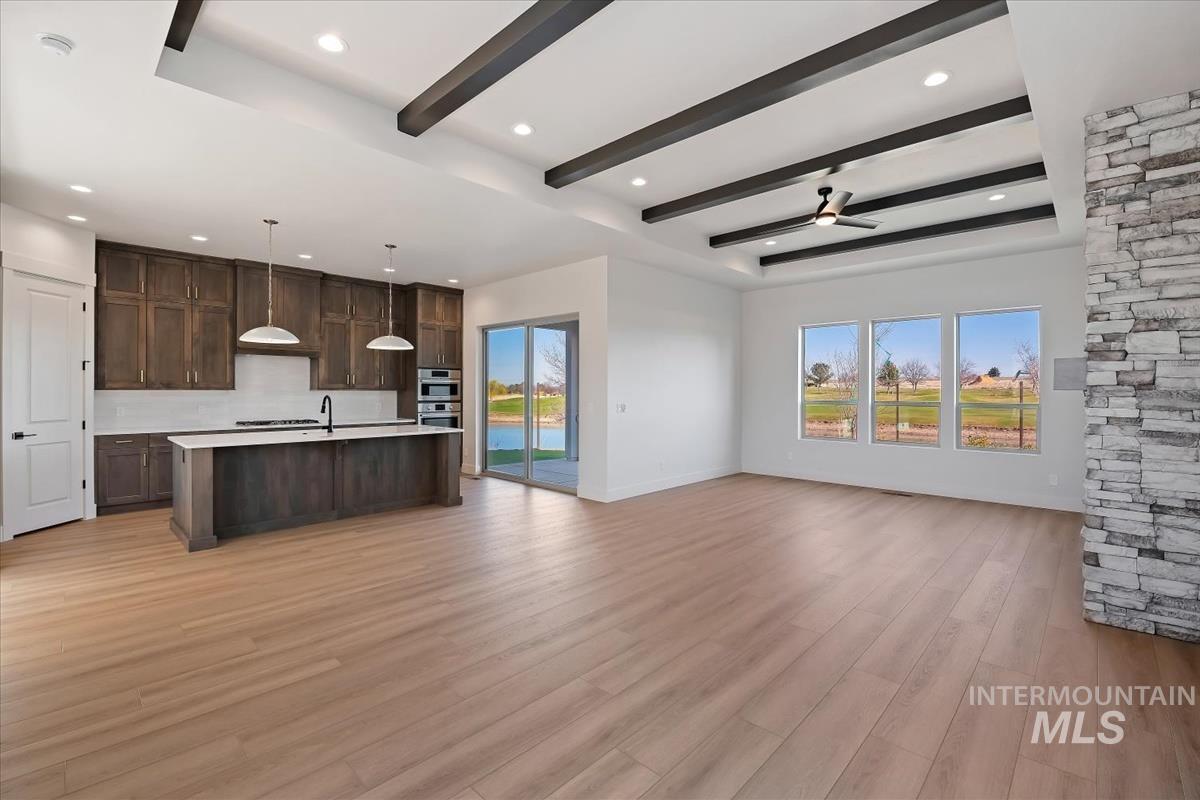 Kitchen featuring open floor plan, dark wood finish cabinetry, an island with sink, light wood-style flooring, and pendant lighting