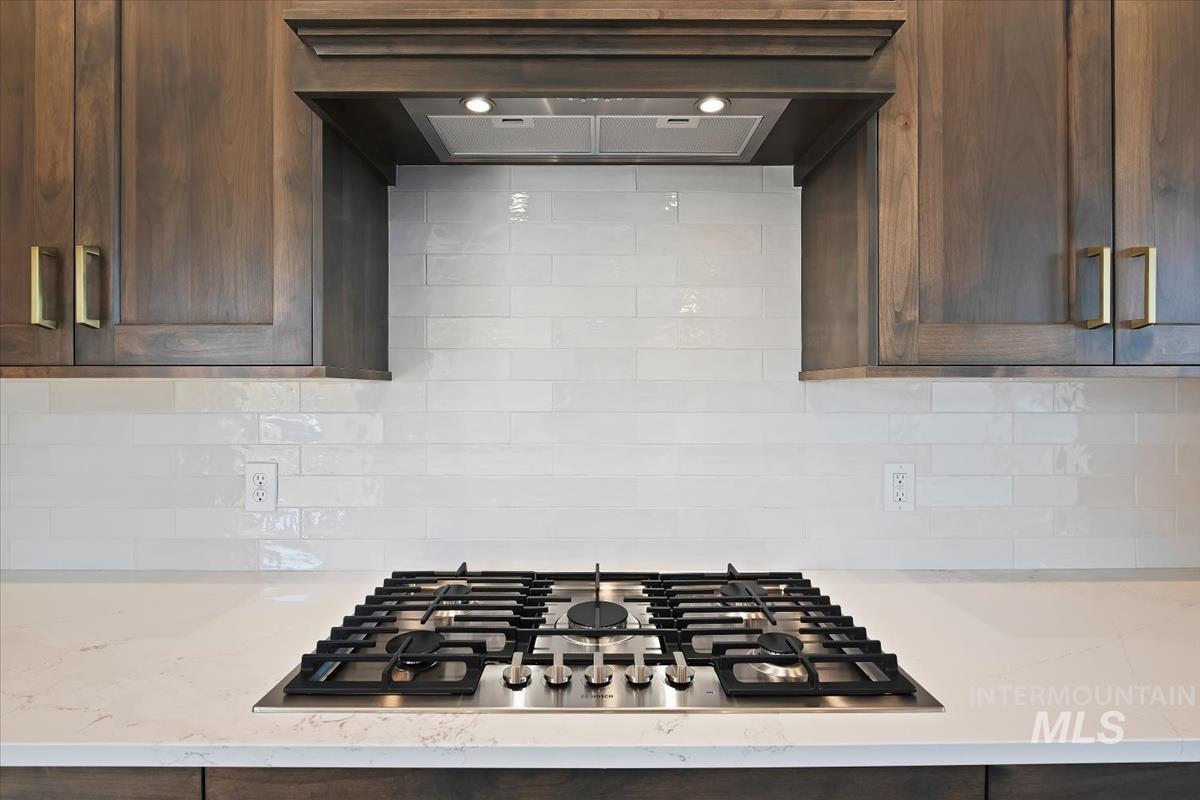 Kitchen featuring stainless steel gas stovetop, dark wood finish cabinets, light stone counters, and backsplash