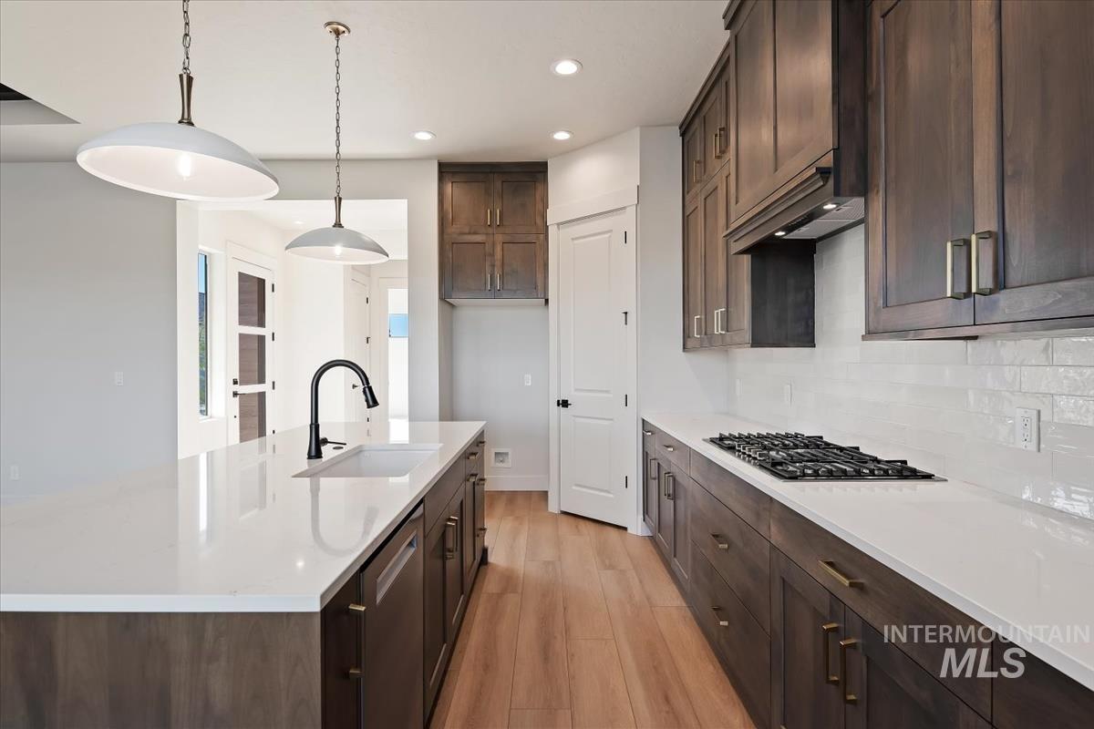 Kitchen featuring dark wood finish cabinetry, light wood finished floors, light stone countertops, and stainless steel appliances