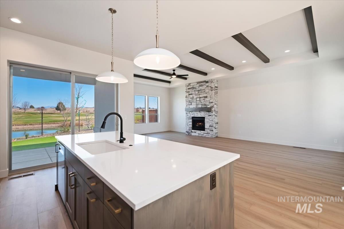 Kitchen with pendant lighting, open floor plan, a center island with sink, a water view, and light wood-style floors