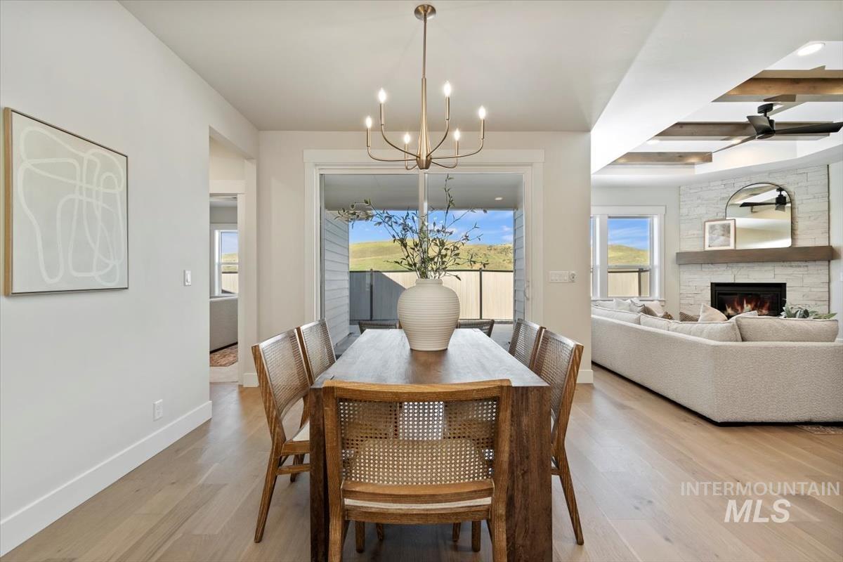 Dining area with a chandelier, light wood finished floors, a fireplace, and ceiling fan