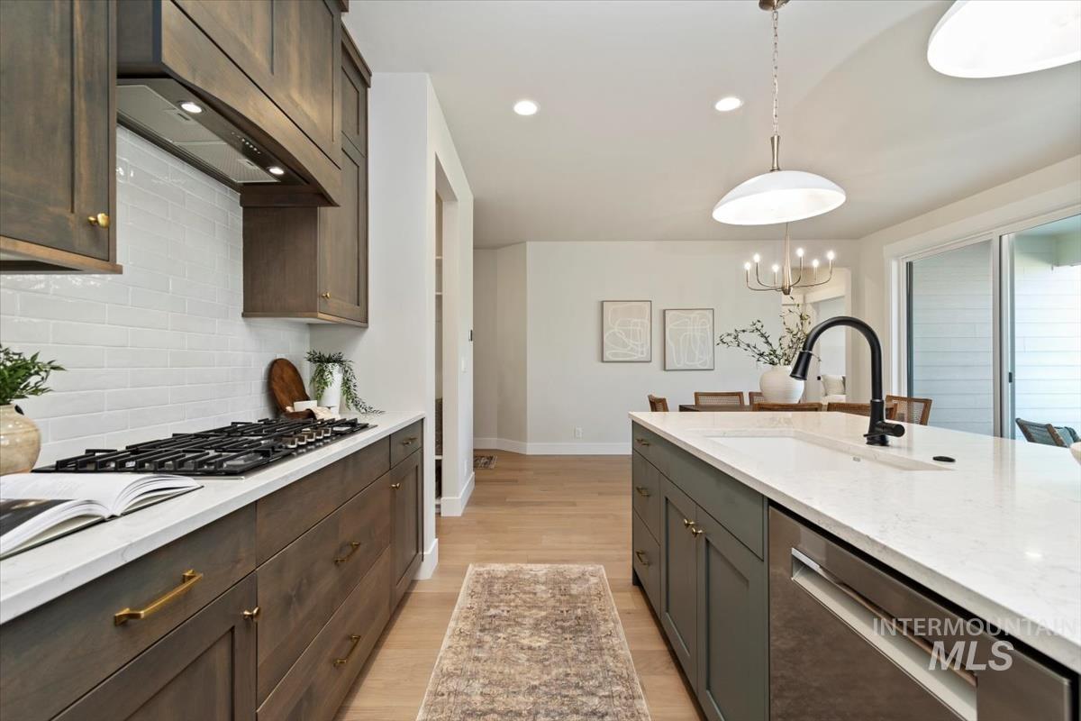 Kitchen with stainless steel appliances, tasteful backsplash, dark brown cabinets, light wood-style floors, and wall chimney range hood