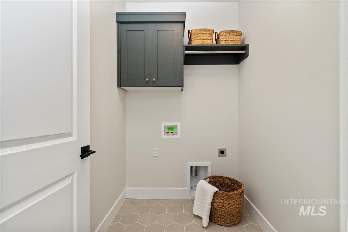 Washroom featuring hookup for an electric dryer, hookup for a washing machine, light tile patterned floors, and cabinet space