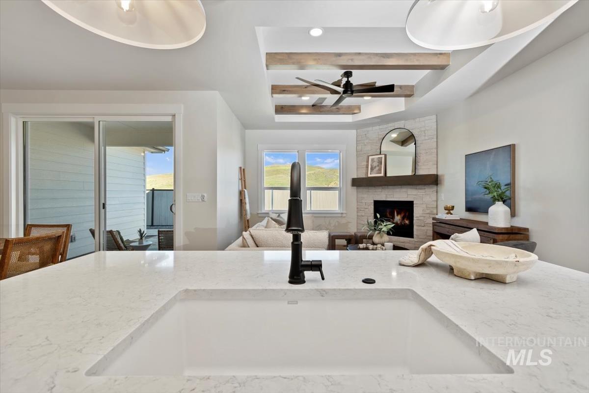 Kitchen with ceiling fan, a fireplace, light stone counters, and beamed ceiling