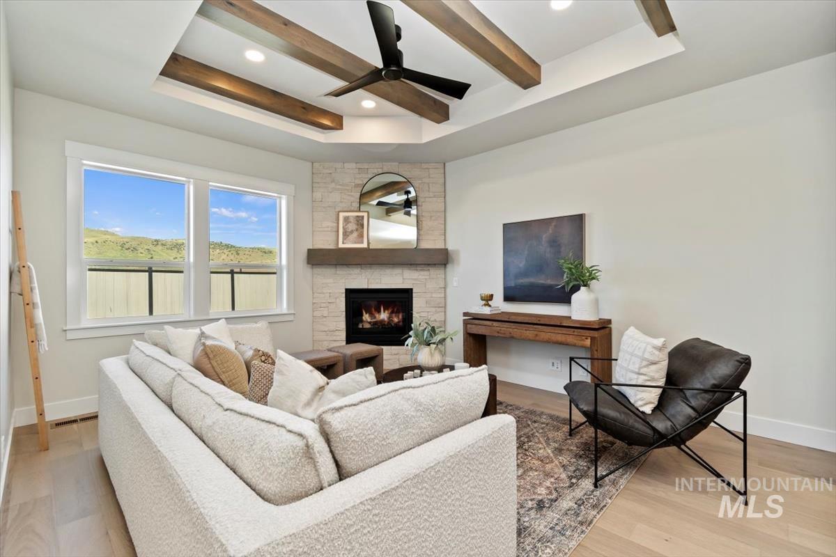 Living room featuring ceiling fan, light wood-type flooring, a fireplace, a tray ceiling, and beam ceiling