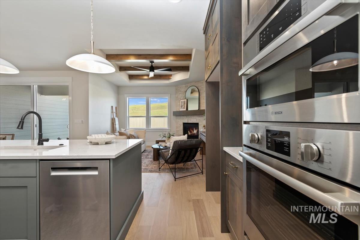Kitchen with appliances with stainless steel finishes, light countertops, light wood-style flooring, a large fireplace, and coffered ceiling