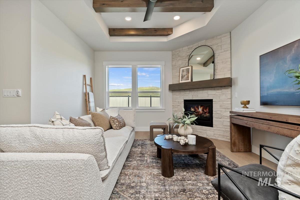 Living room with wood finished floors, a fireplace, a raised ceiling, and a ceiling fan
