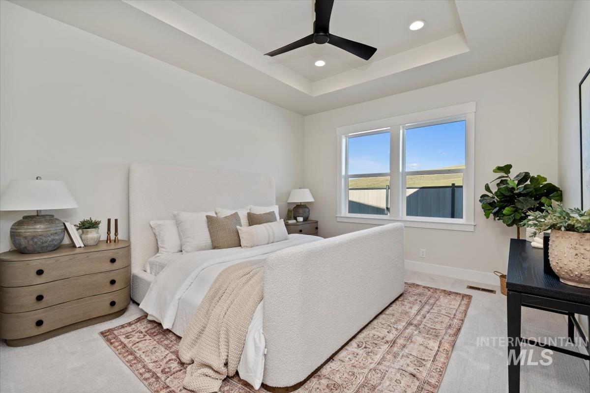 Bedroom with a tray ceiling, light colored carpet, recessed lighting, and ceiling fan