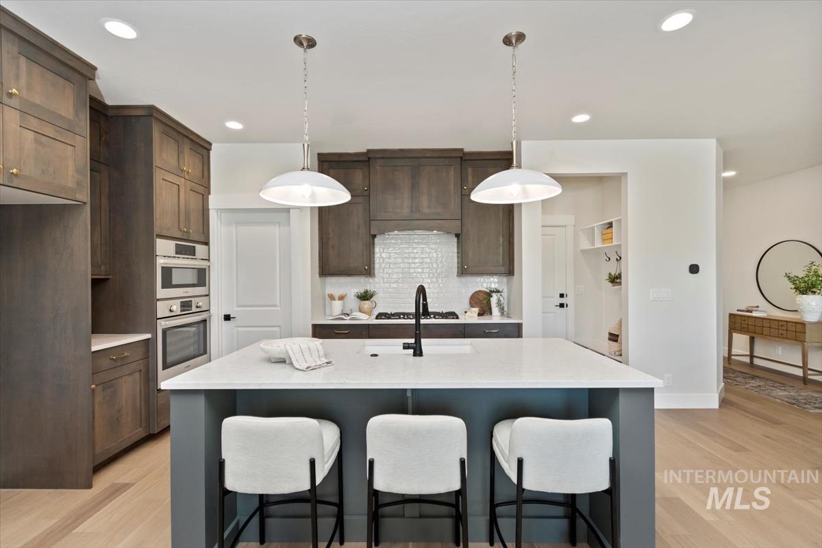 Kitchen with light wood-style floors, backsplash, a breakfast bar, recessed lighting, and dark brown cabinets