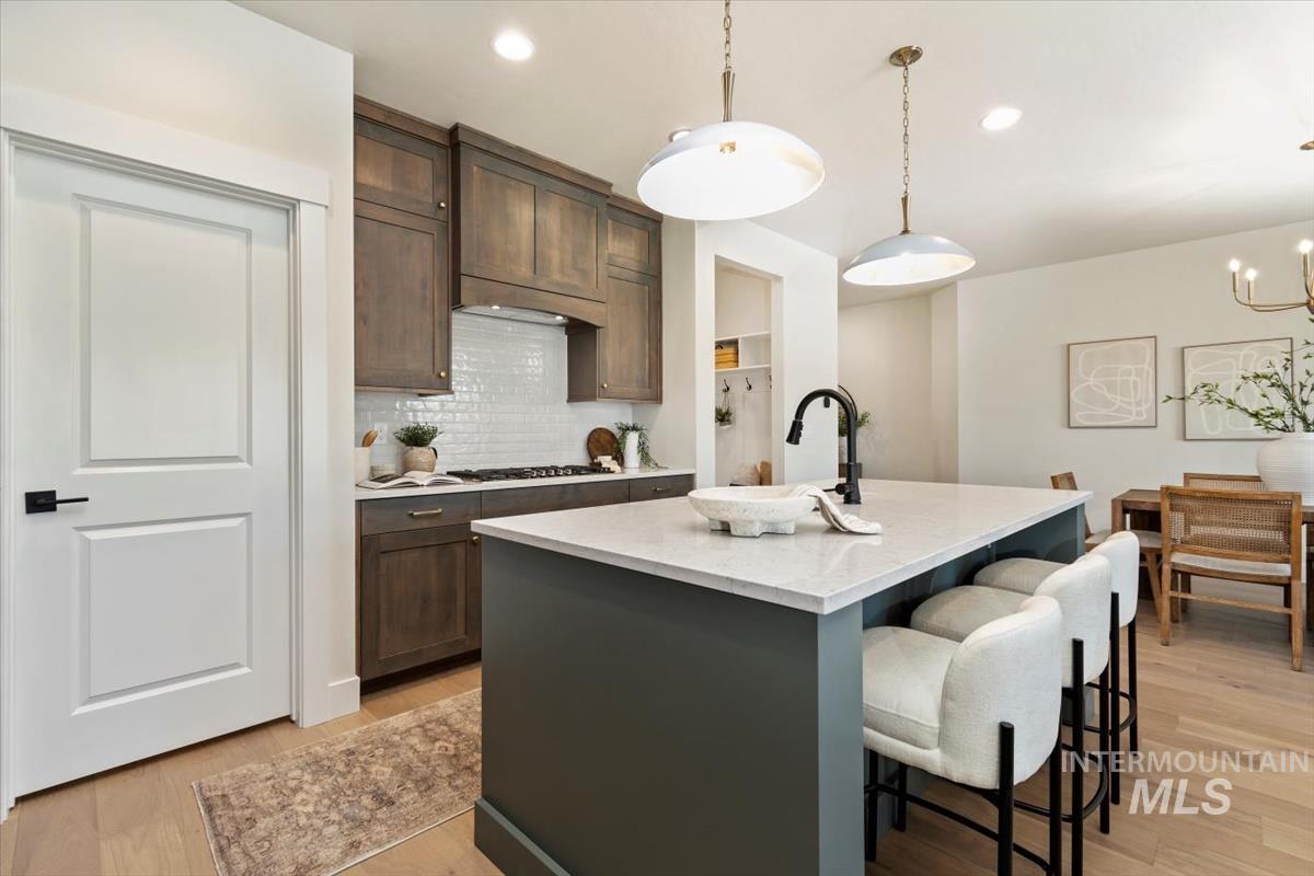Kitchen featuring a kitchen breakfast bar, tasteful backsplash, a kitchen island with sink, light wood-style flooring, and dark brown cabinets