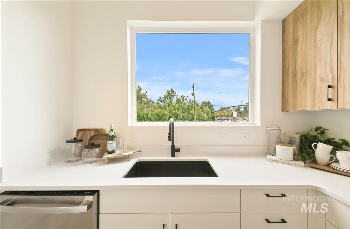 Kitchen featuring stainless steel dishwasher, light countertops, and white cabinets