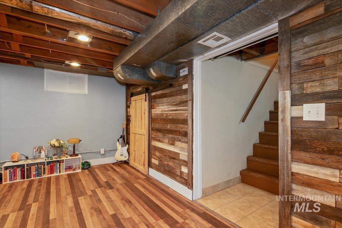 Finished below grade area with wooden walls, a barn door, stairway, and wood finished floors