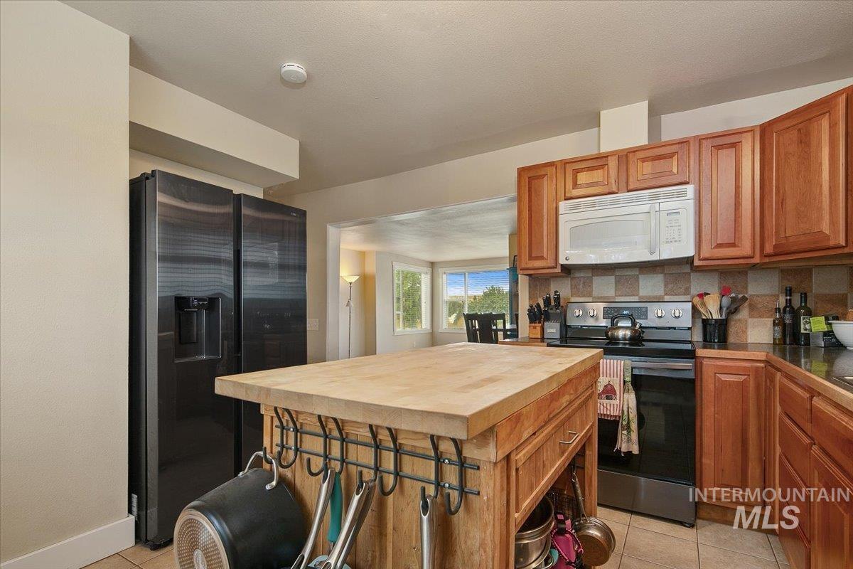 Kitchen featuring butcher block counters, black fridge with ice dispenser, stainless steel electric range, light tile patterned flooring, and brown cabinetry