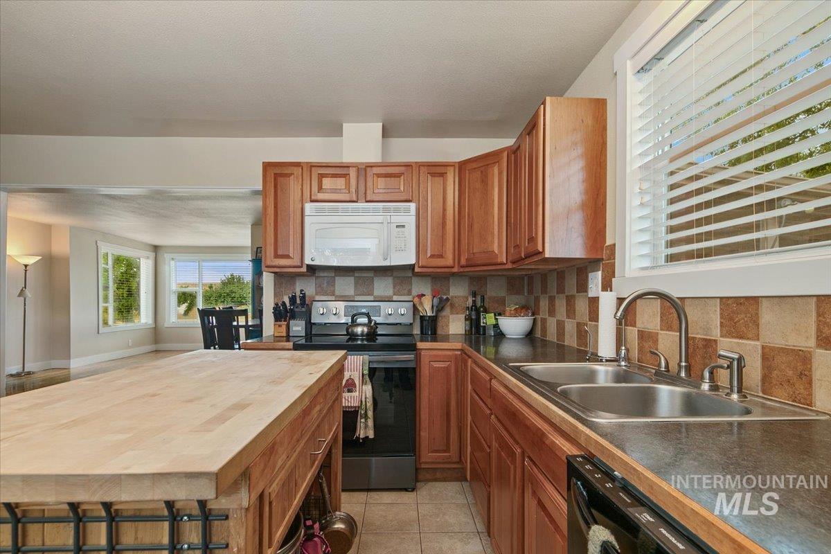Kitchen with stainless steel range with electric cooktop, backsplash, white microwave, light tile patterned floors, and dishwasher