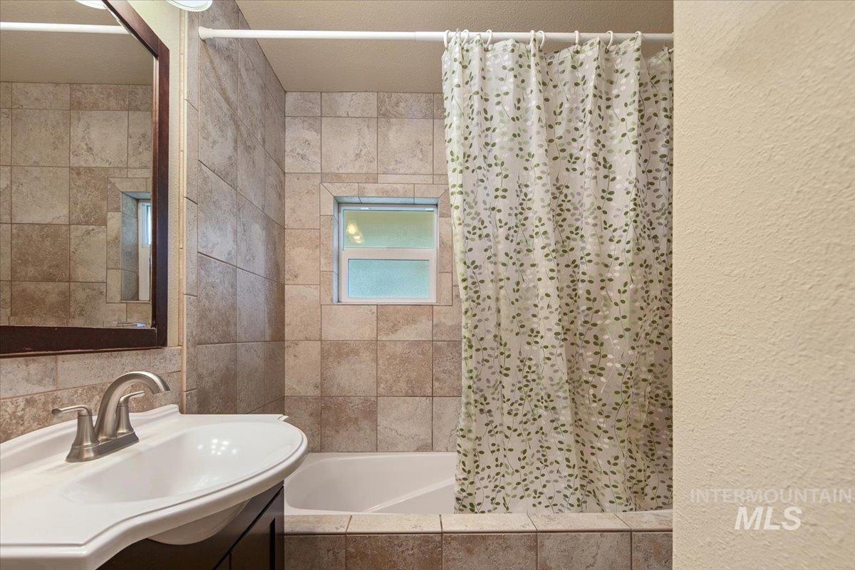 Bathroom featuring vanity, tiled shower / bath combo, tile walls, and a textured wall