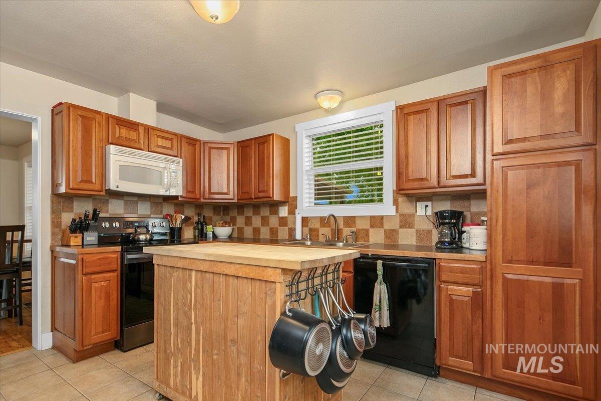 Kitchen with decorative backsplash, black appliances, light tile patterned flooring, brown cabinetry, and a textured ceiling