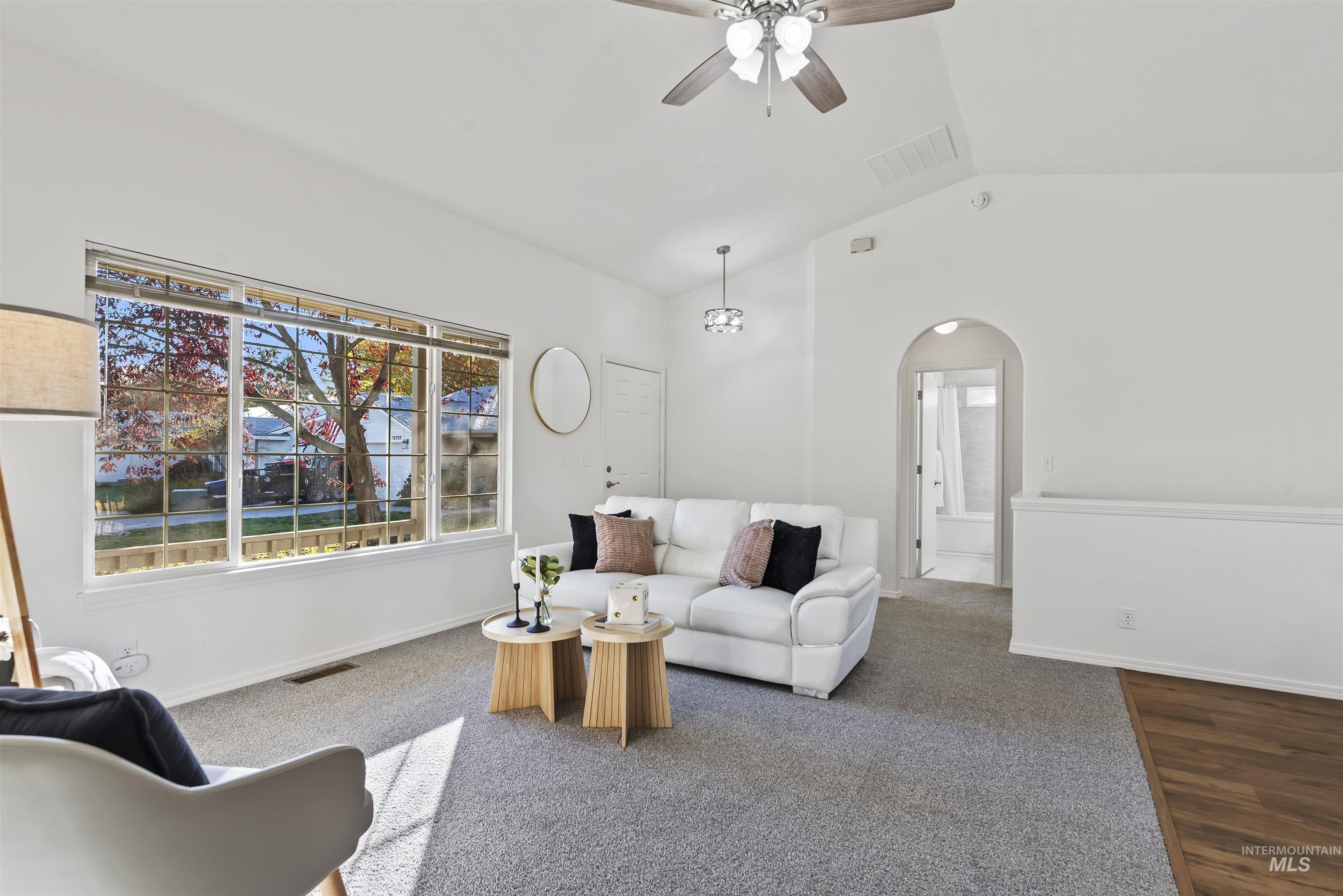 Living room featuring lofted ceiling, a ceiling fan, carpet floors, arched walkways, and wood finished floors