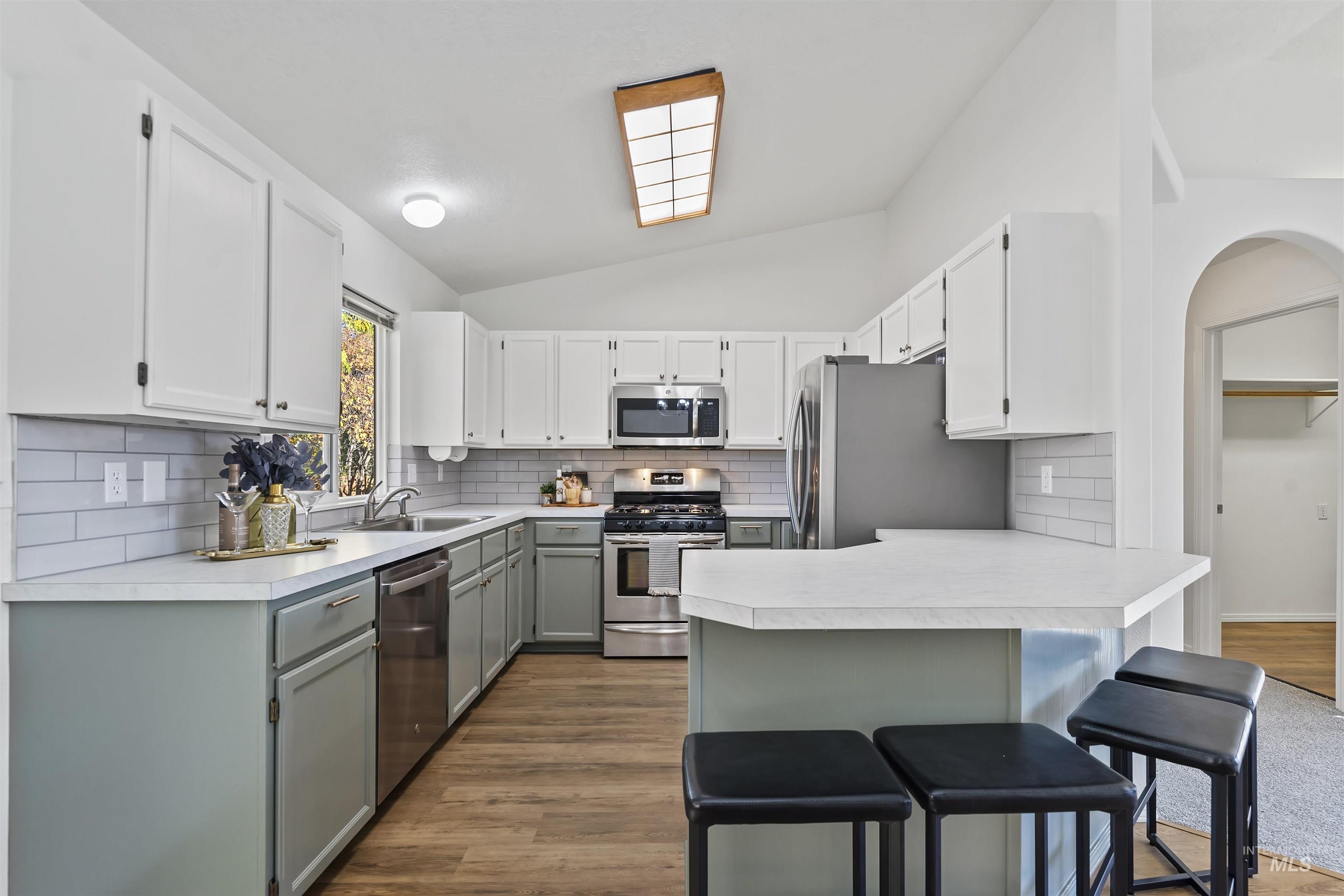 Kitchen with backsplash, light countertops, a breakfast bar, a peninsula, and appliances with stainless steel finishes