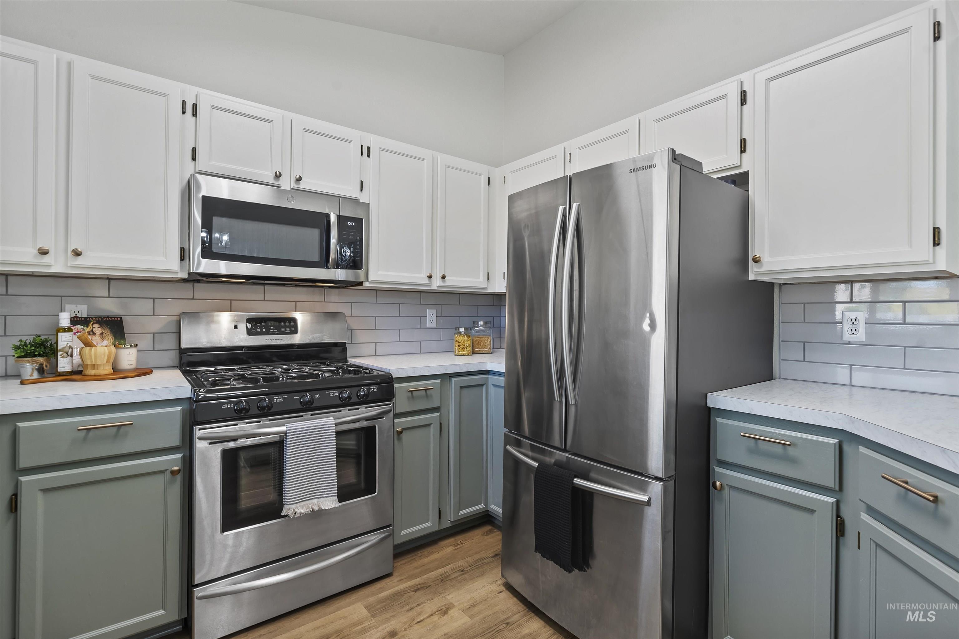 Kitchen with stainless steel appliances, light countertops, backsplash, and gray cabinets